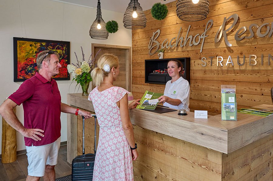 Zwei Gäste stehen vor der Rezeption vom Bachhof Resort in Straubing und Sprechen mit einer Dame hinter der Rezeption